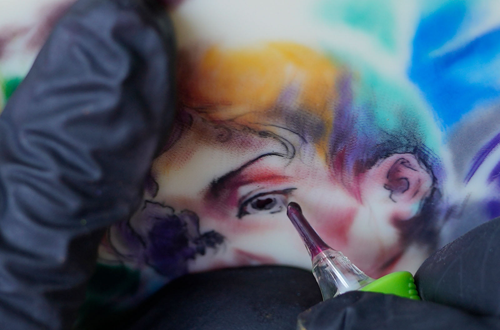 Tattoo artist using Regal tattoo ink to shade a colorful portrait tattoo with a cartridge needle in a close-up studio shot.